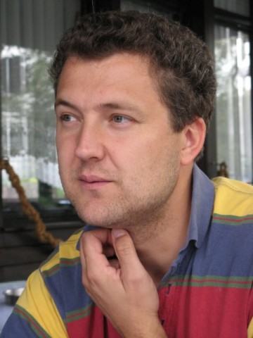 Foto de Irfan Skiljan. Homem branco, com a mão esquerda no queixo, vestindo camisa azul, amarela e vermelha.