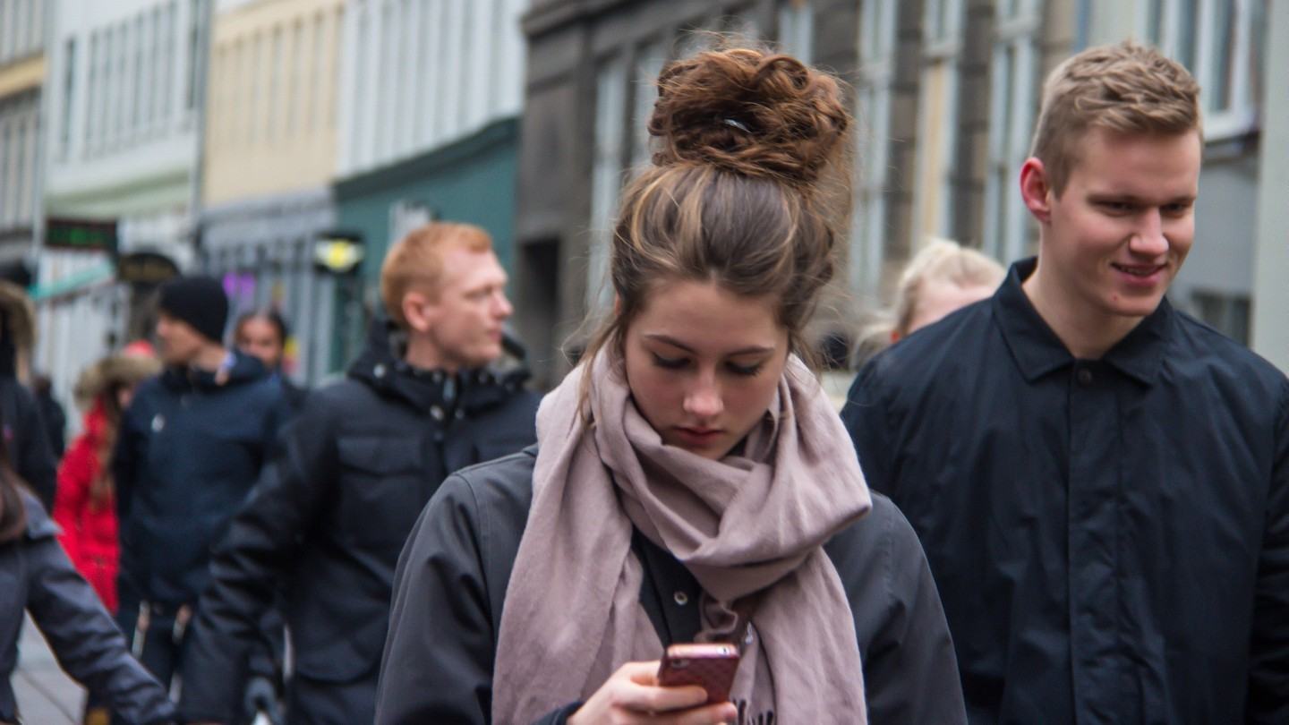Mulher olhando o celular enquanto anda na rua.