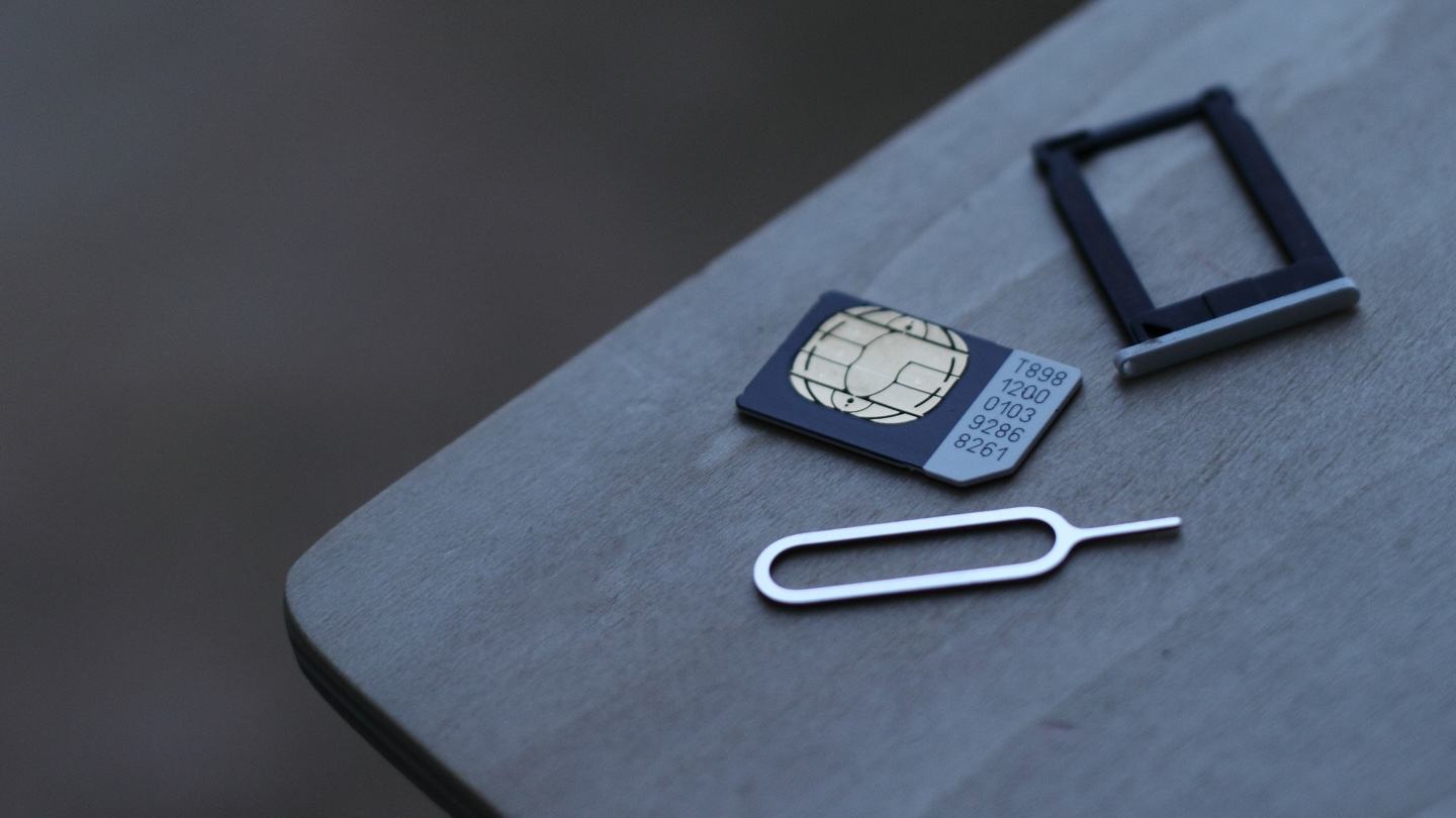 SIM card, bandeja de celular e clipe em cima de uma mesa.