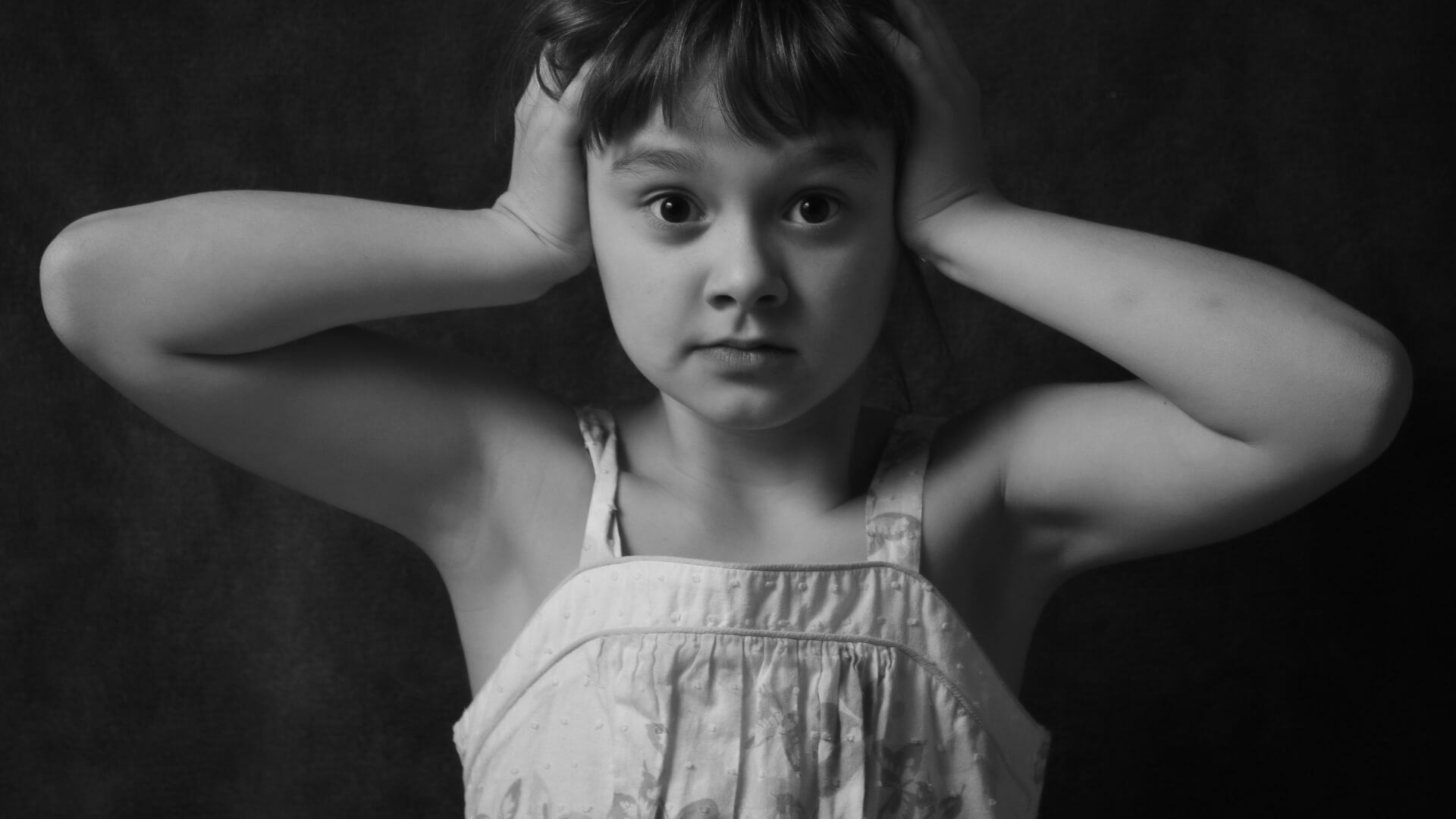 Menina com as mãos nas orelhas e cara de assustada.