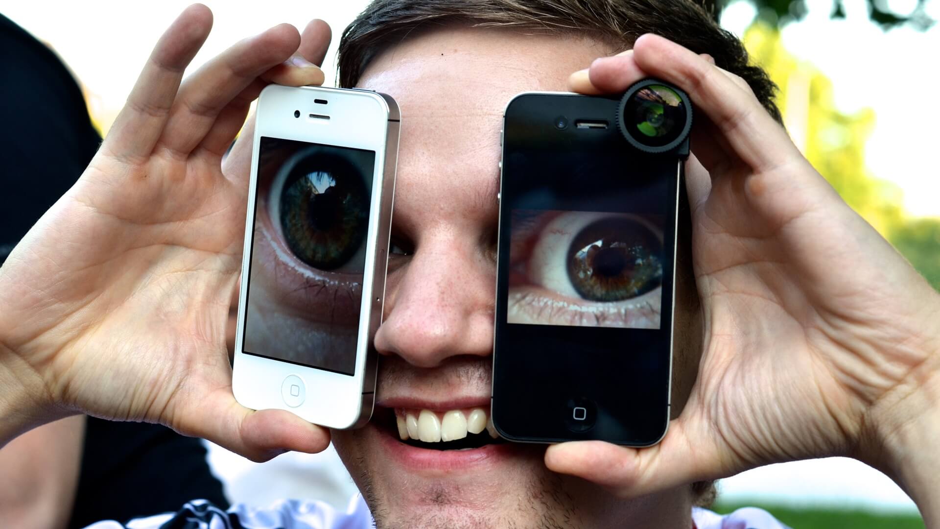 Homem segurando dois iPhones nos olhos com a tela ligada exibindo olhos enormes.