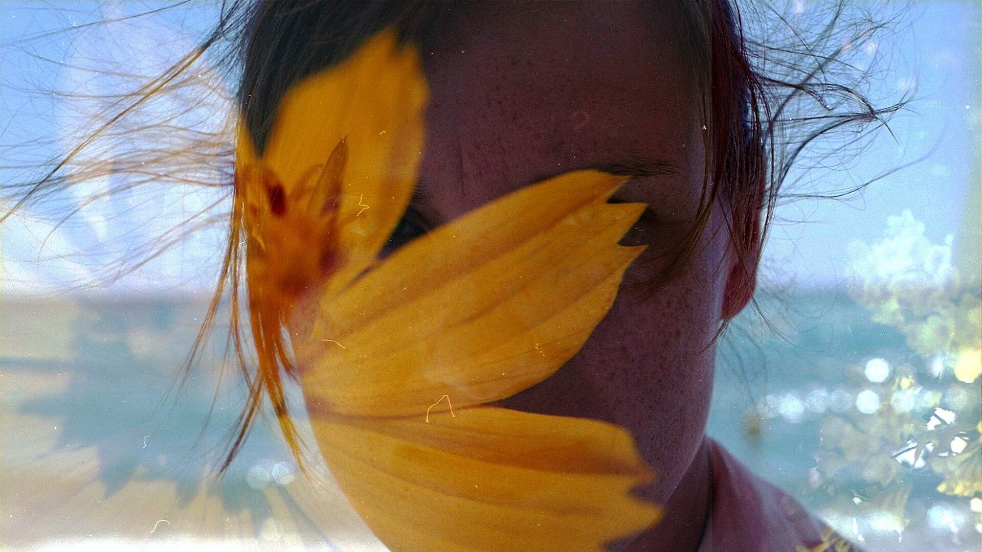 Rosto de uma mulher coberto por flor amarela em foto com dupla exposição.