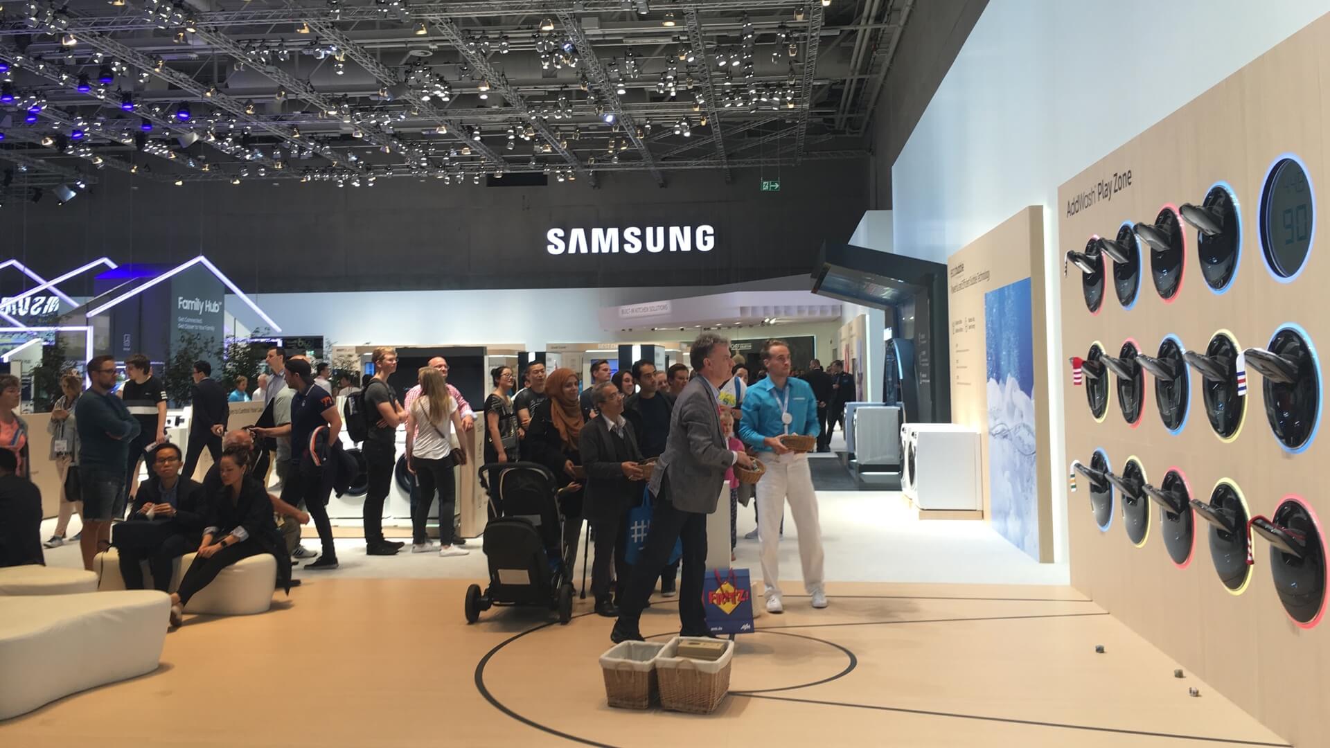 Pessoas comuns na IFA em torno de um game no estande da Samsung.