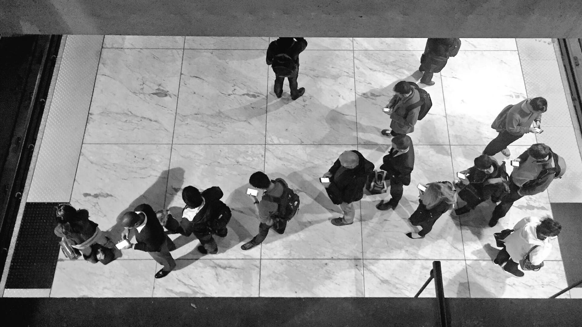 Pessoas em fila olhando para seus smartphones.