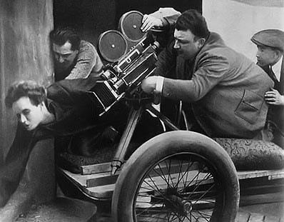 Operadora de câmera sobre um carrinho, manuseando uma câmera grande.