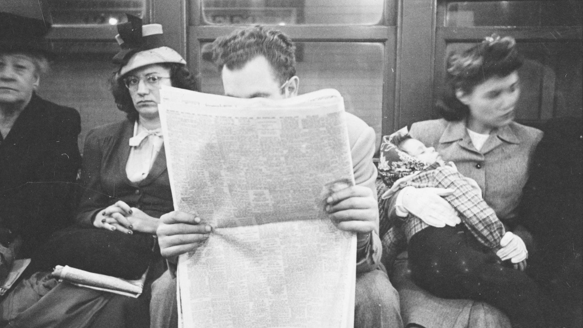 Homem lê jornal sentado em trem do metrô de Nova York.