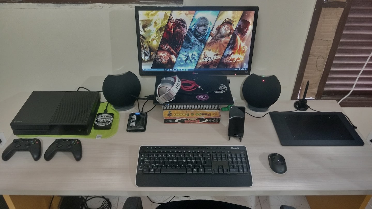 Mesa com monitor, teclado e mouse, caixas de som e alguns acessórios.