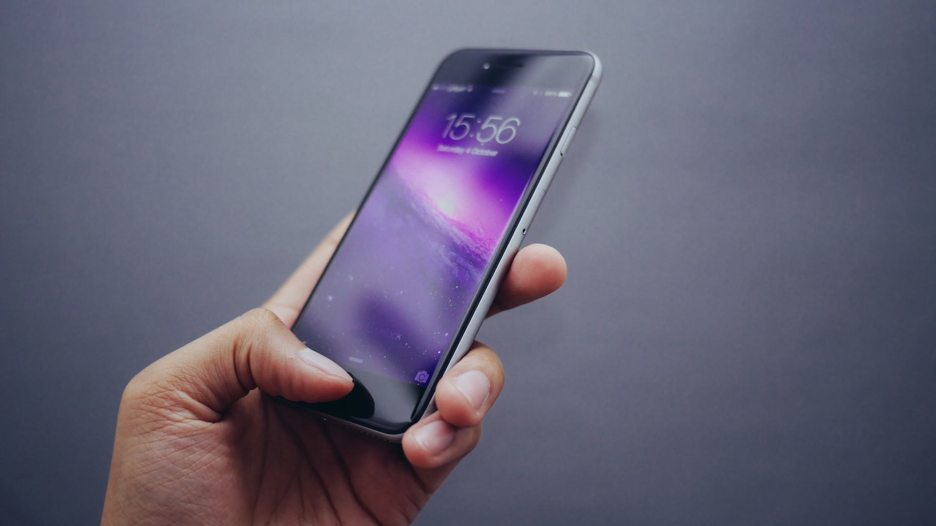 Mão segurando um iPhone com o polegar sobre o sensor de digitais.