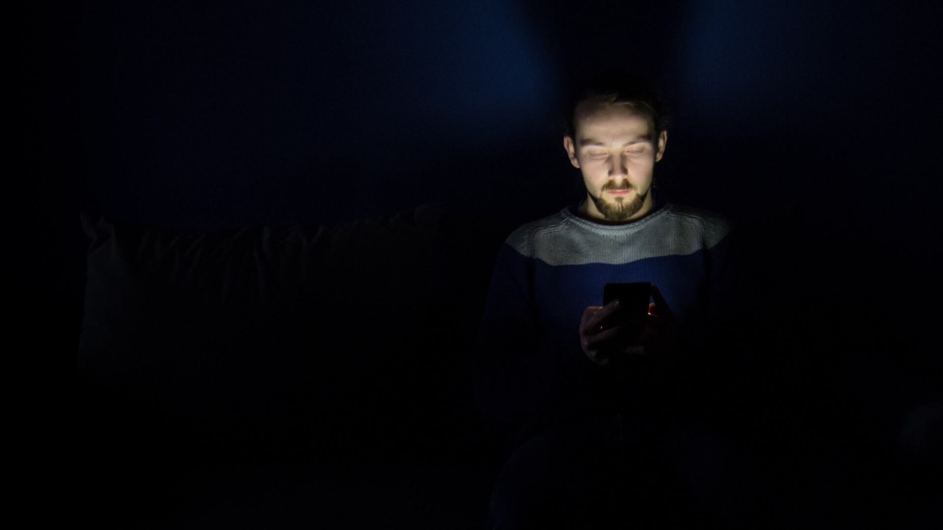 Homem no escuro mexendo em um celular com brilho elevado.