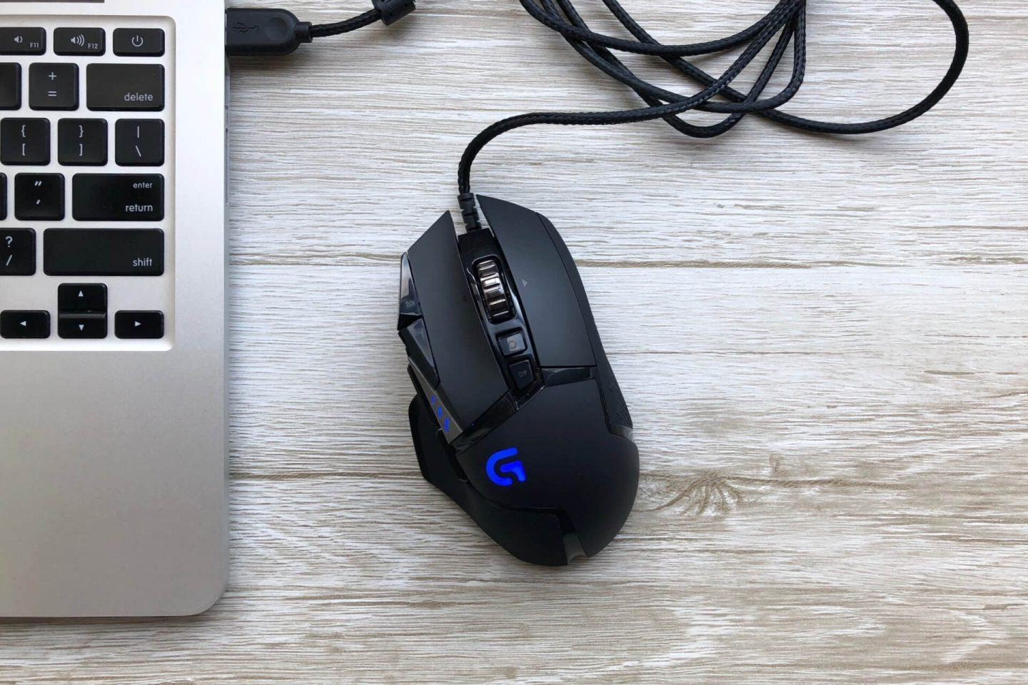 Visão aérea do mouse Logitech G502 ao lado de um notebook.
