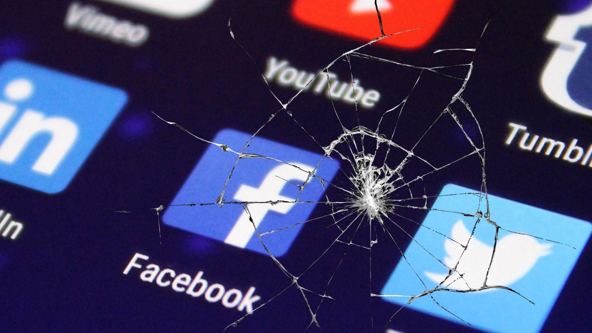 Ícones de redes sociais vistos através de uma tela trincada.