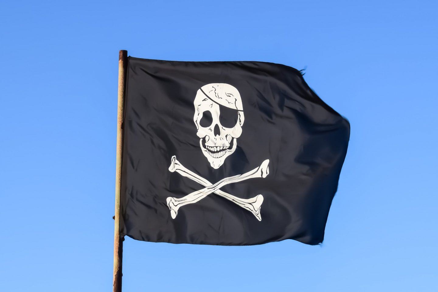 Bandeira pirata hasteada e tremulando contra céu azul.