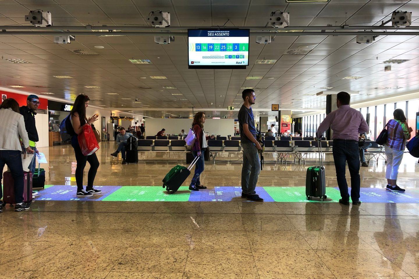 Pessoas aguardam em uma fila, iluminadas pelos projetores da solução high-tech da Azul e Infraero.