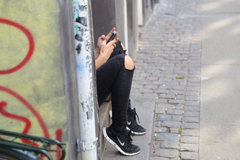 Mulher em uma calçada com parte do corpo escondida mexendo em um celular.
