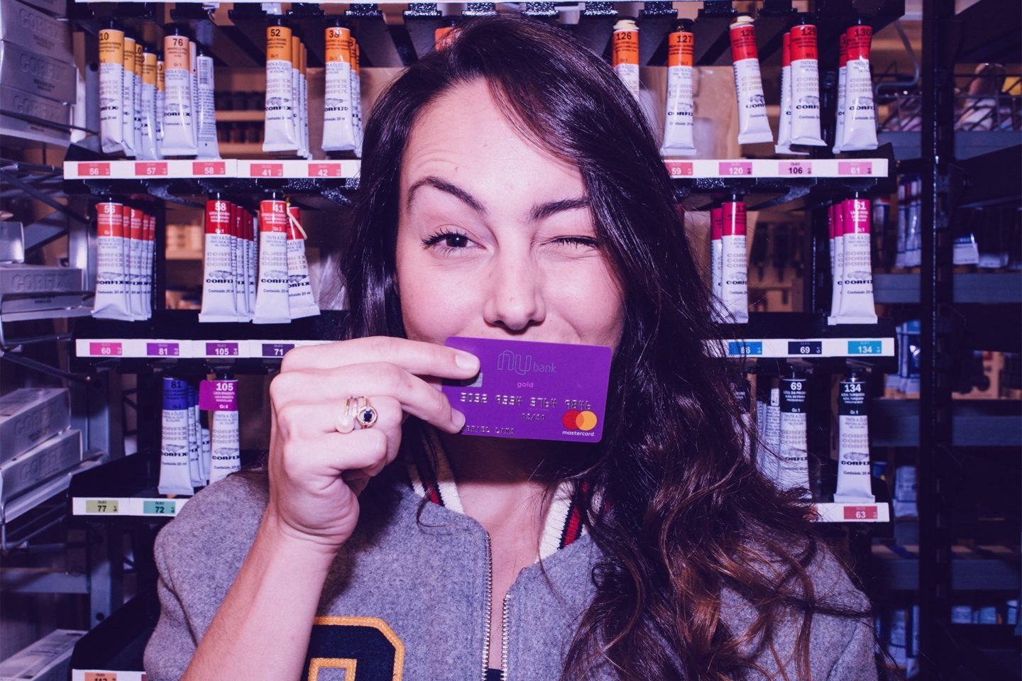 Mulher segurando cartão do Nubank na altura da boca e piscando um dos olhos.