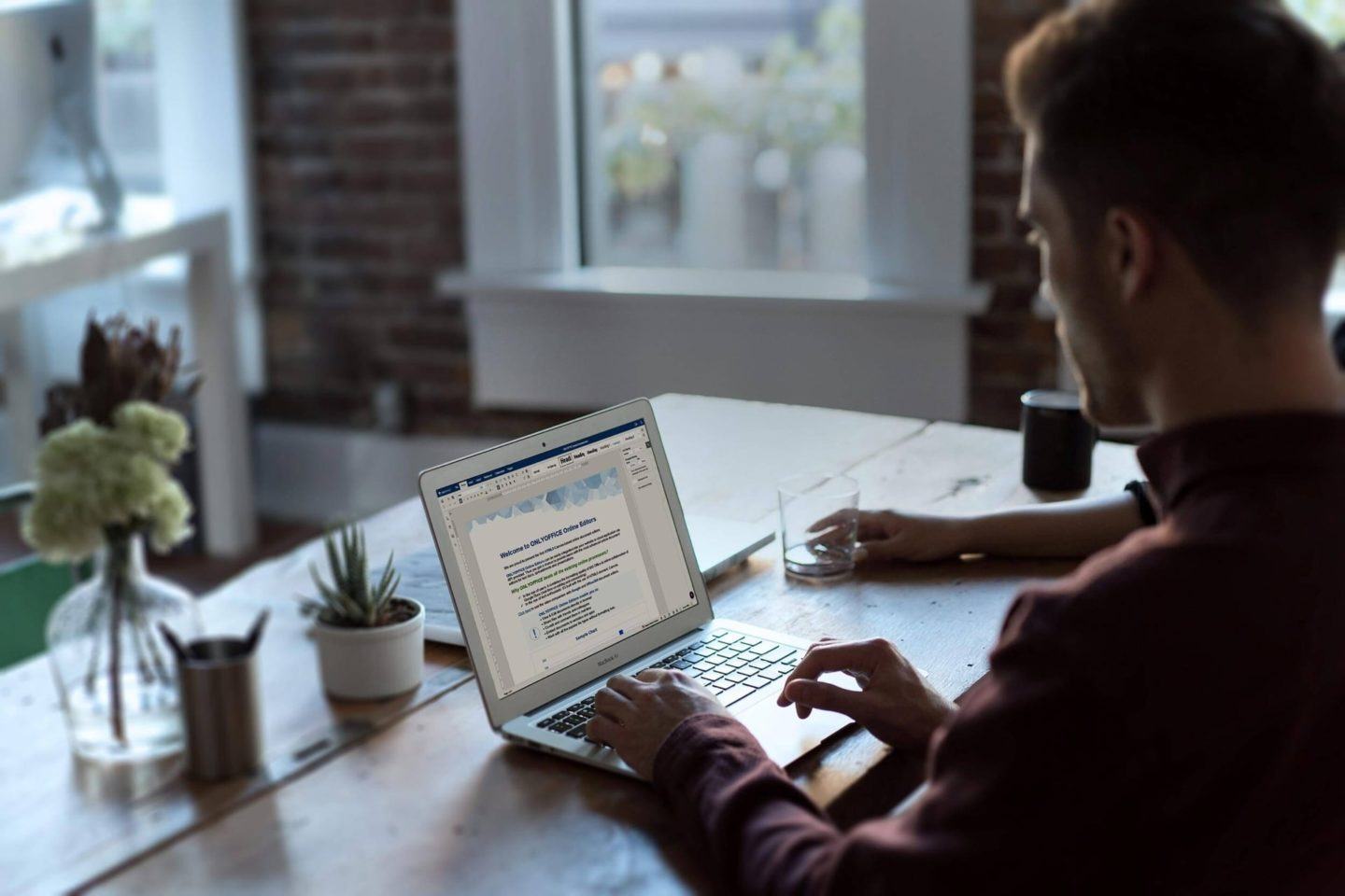 Homem de costas digitando em um notebook com um documento aberto no OnlyOffice.
