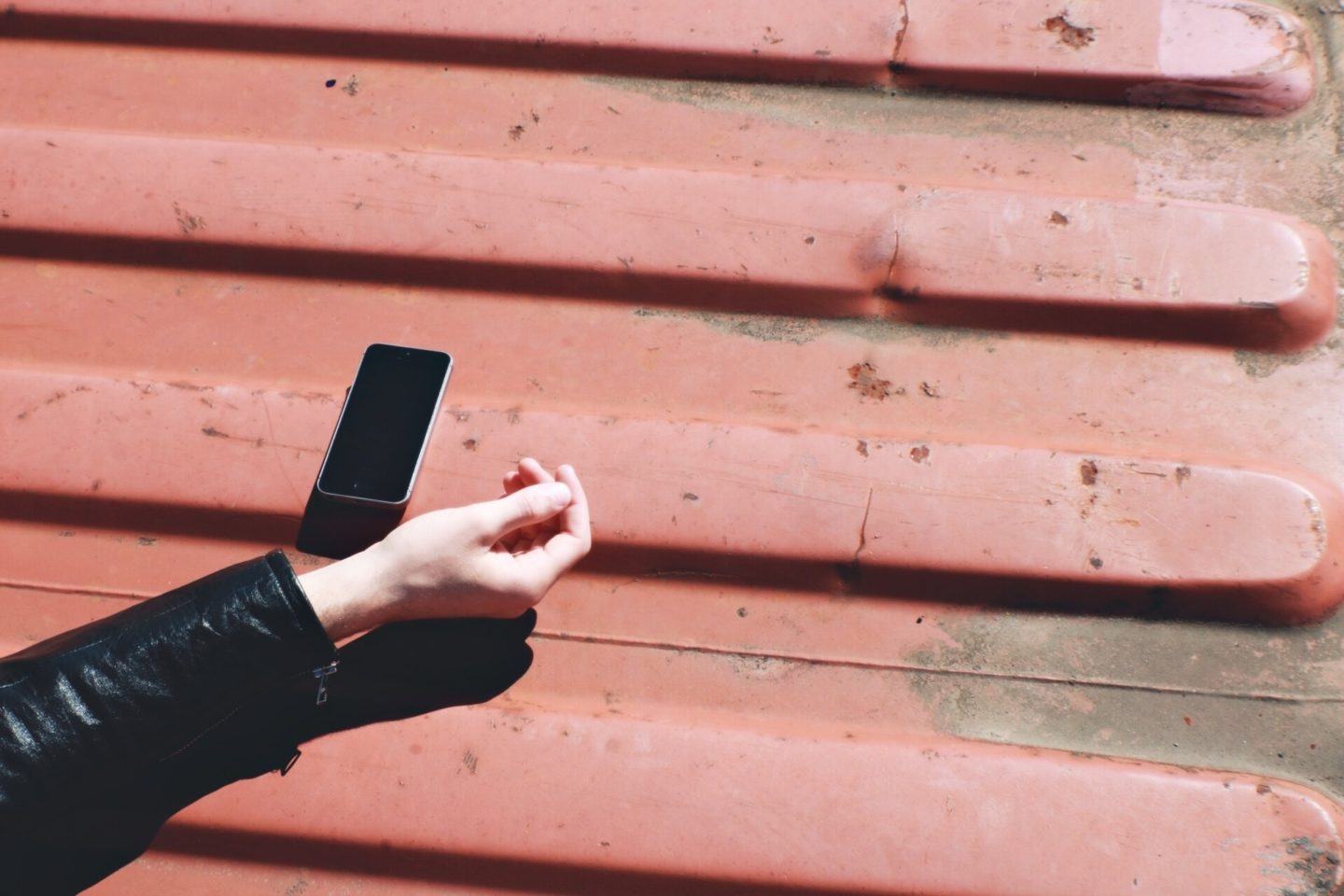 Braço com um celular ao lado sobre uma superfície vermelha ensolarada.
