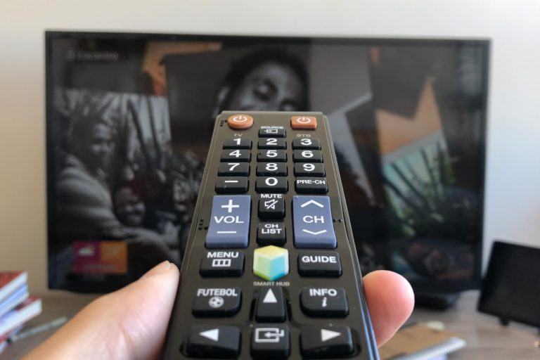Controle de TV em frente a uma TV ligada.
