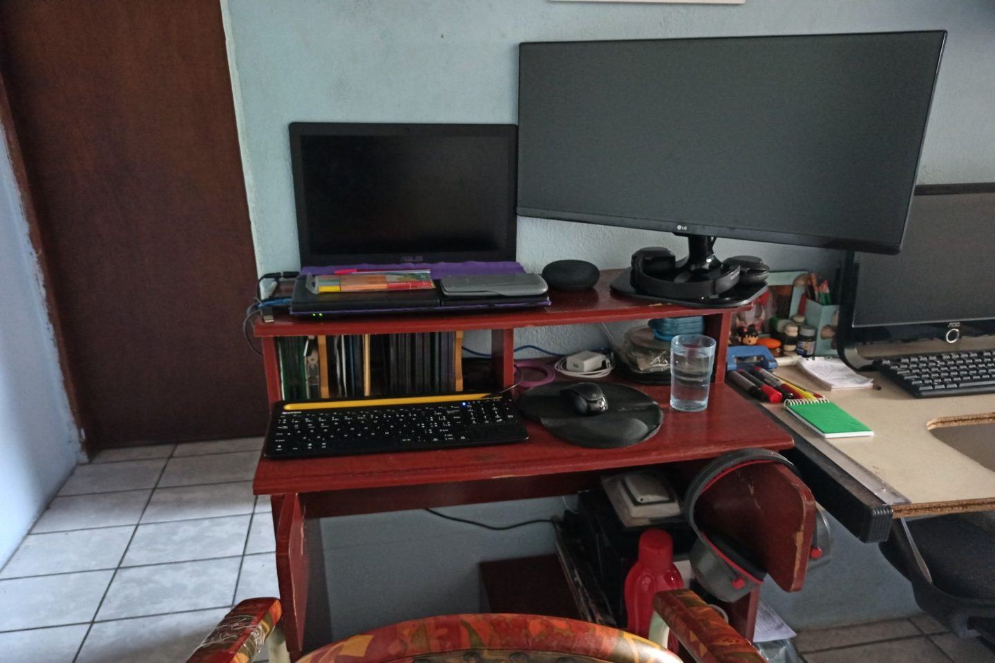 Escritório doméstico do Henrique Bispo, mostrando um rack com notebook, teclado e mouse; um monitor grande e alguns objetos.