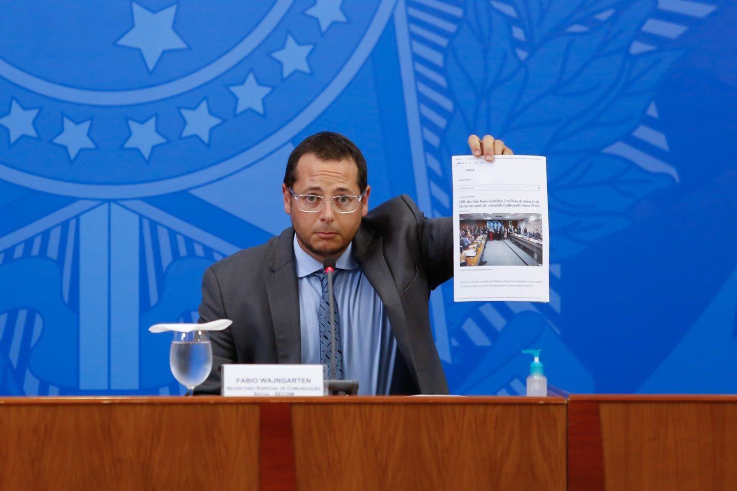 Fábio Wajngarten segurando uma folha impressa sentado à mesa.