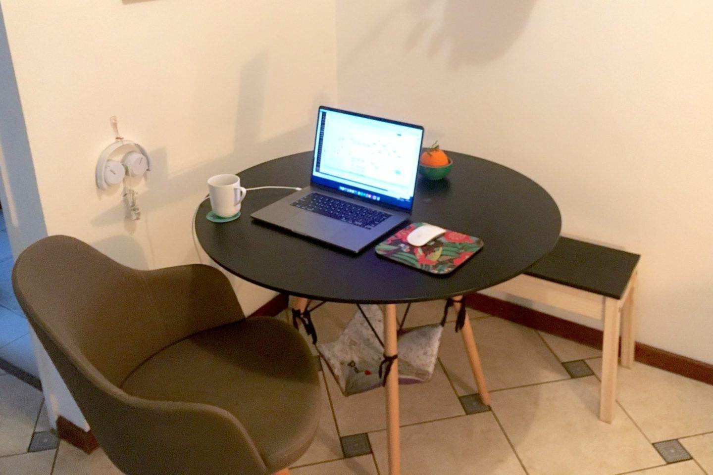 Poltrona e mesa de jantar com um notebook, mouse e caneca sobre ela.