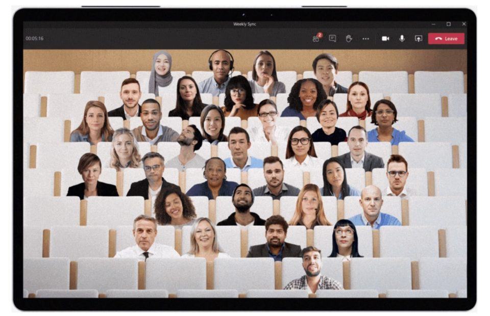 Tela de um tablet mostrando o Microsoft Teams em uma videochamada com várias cabeças de pessoas em uma espécie de auditório virtual.