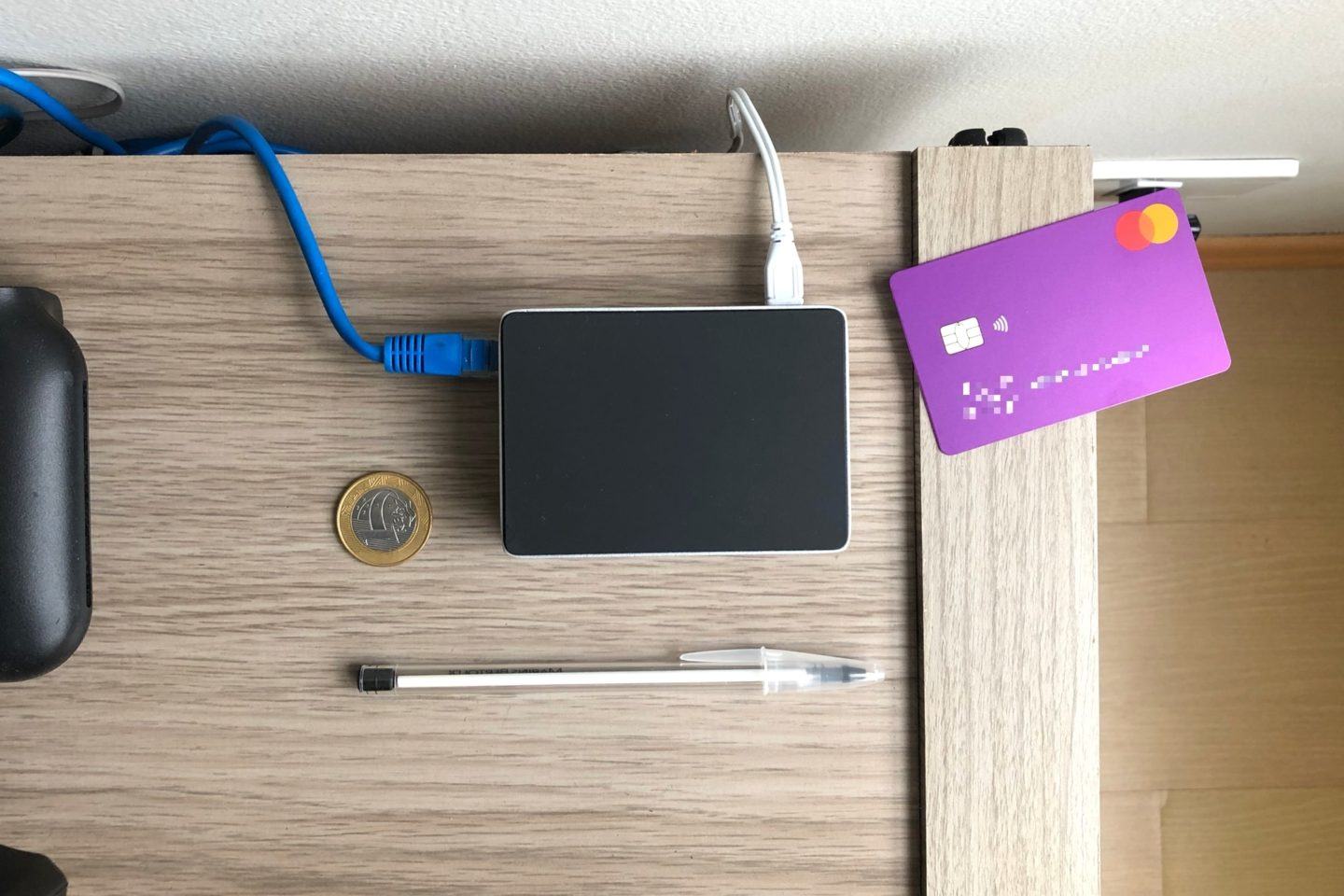 Foto de cima do Raspberry Pi, rodeado por um cartão de crédito roxo, uma moeda de R$ 1 e uma caneta.