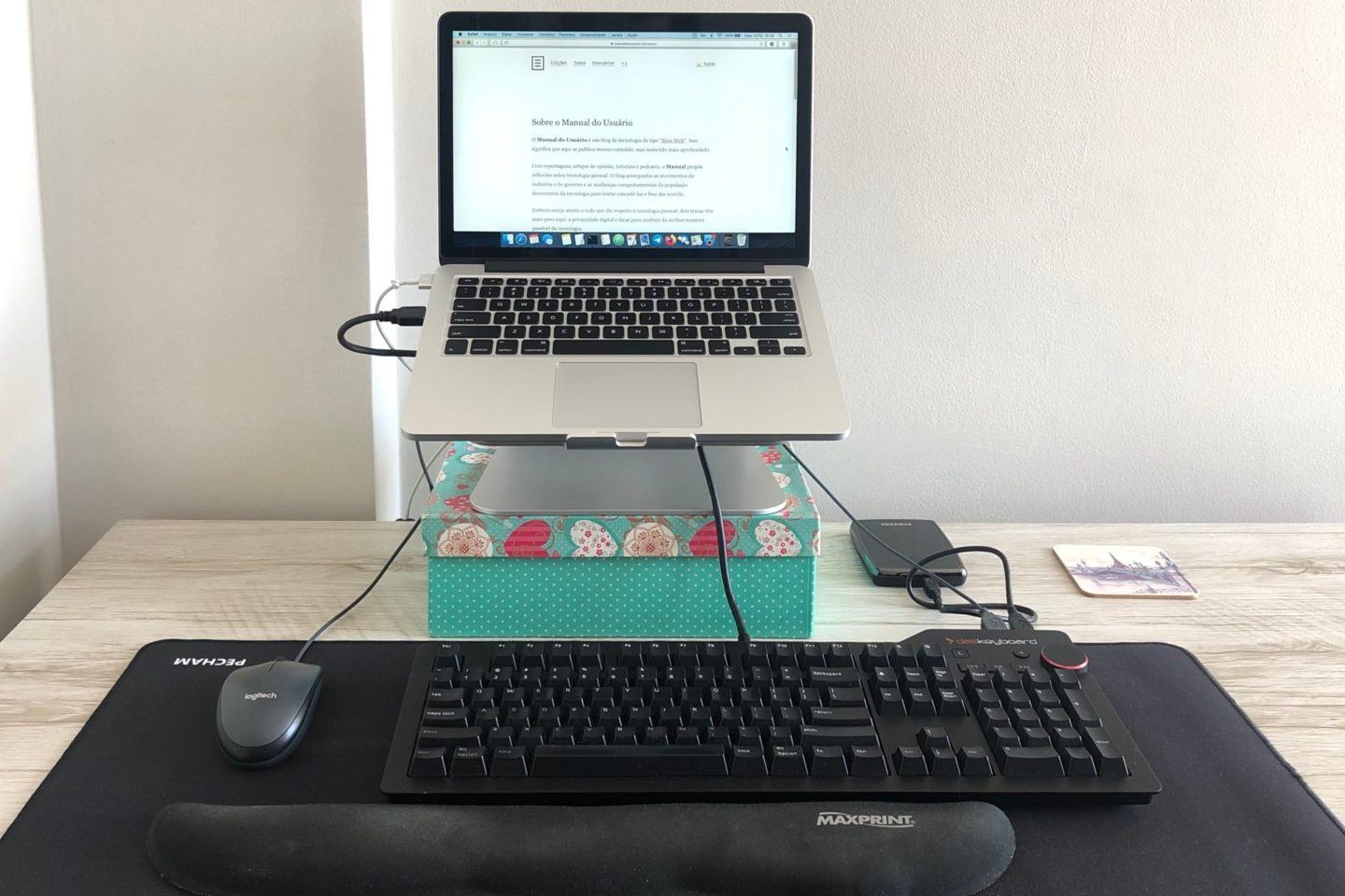 Foto de um notebook elevado sobre uma caixa verde, com fios ligando um mouse, teclado e HD externo.