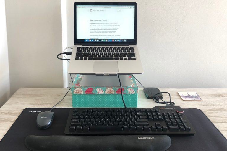 Foto de um notebook elevado sobre uma caixa verde, com fios ligando um mouse, teclado e HD externo.