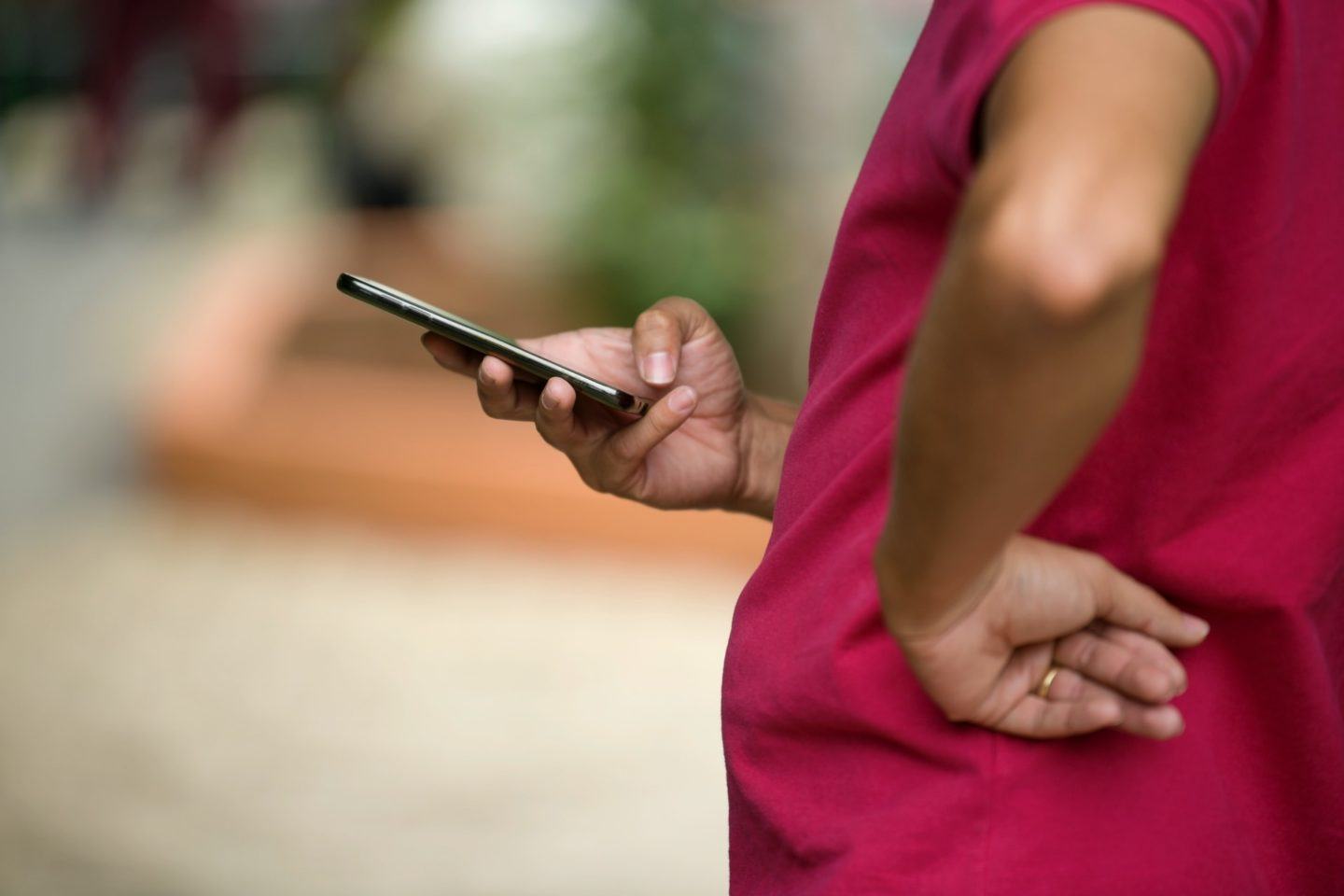 Foto de um homem com a mão na cintura, camisa vermelha, sem mostrar seu rosto. Com a outra mão (direita), ele segura um celular.