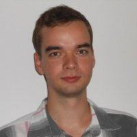 Foto de rosto de um homem branco, cabelo curto e com camisa xadrez, em um fundo branco.