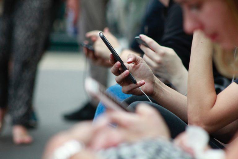 Várias mãos de pessoas enfileiradas segurando/mexendo em celulares.