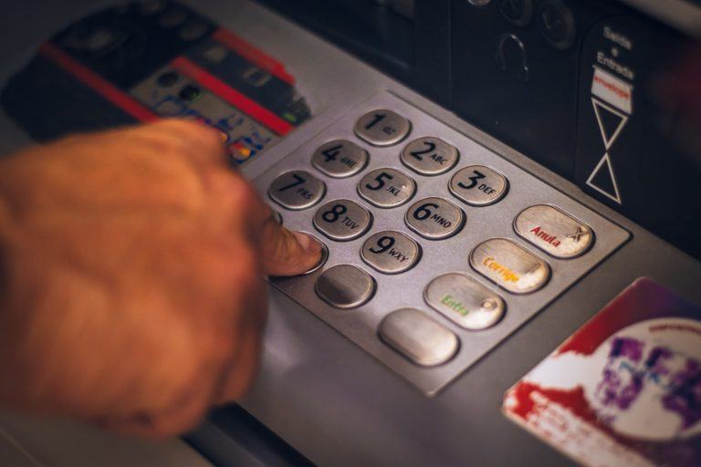 Close em um teclado de caixa eletrônica com uma mão pressionando a tecla zero.