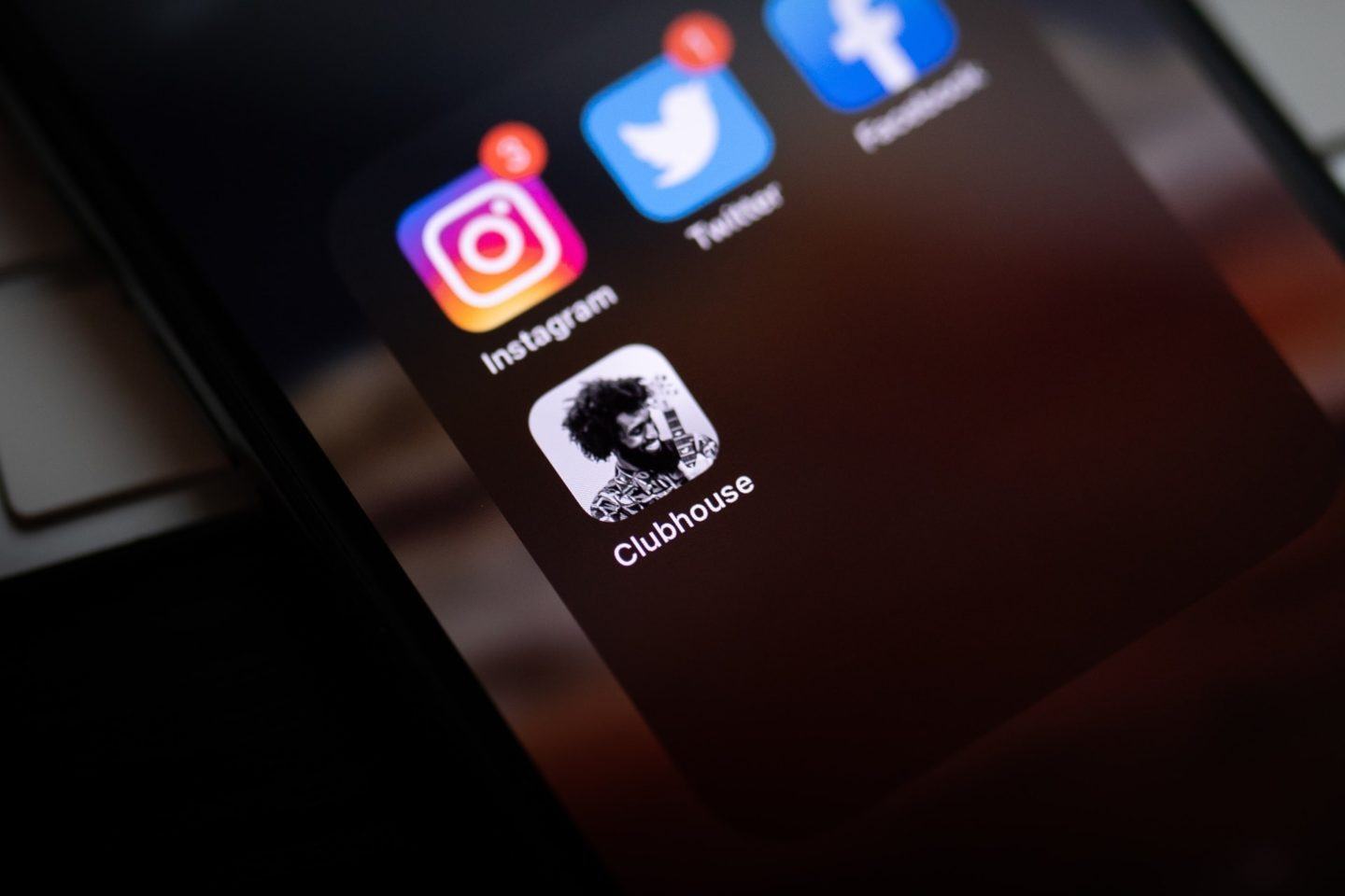 Foto em close de um iPhone num ambiente escuro, com ícones do Clubhouse (em destaque/focado), Instagram, Twitter e Facebook na tela.