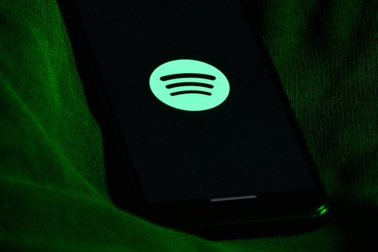 Celular no escuro, com um tecido verde em volta, exibindo o logo do Spotify na tela.