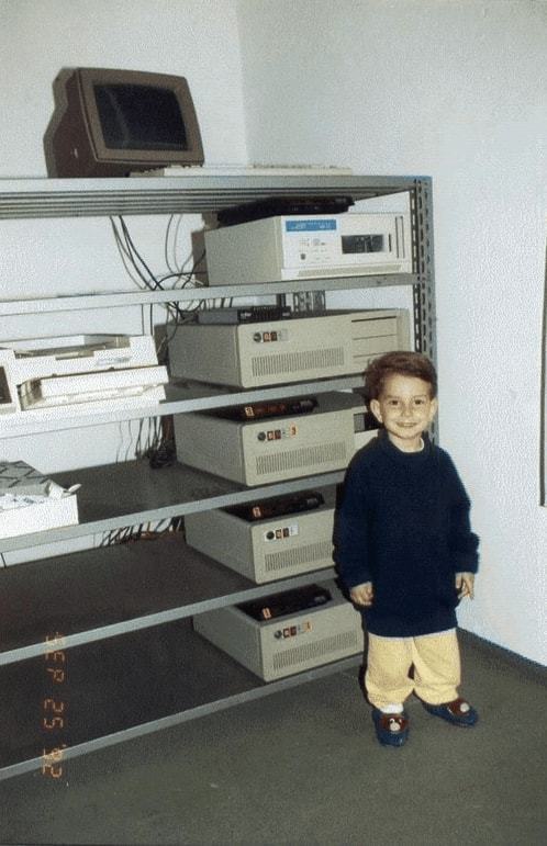 Criança pequena ao lado de uma estante com equipamentos de BBS.