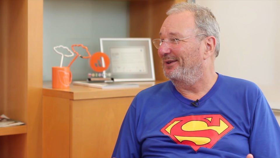 Mandic, de cabelos e barba branca, óculos e sua camiseta do Superman.