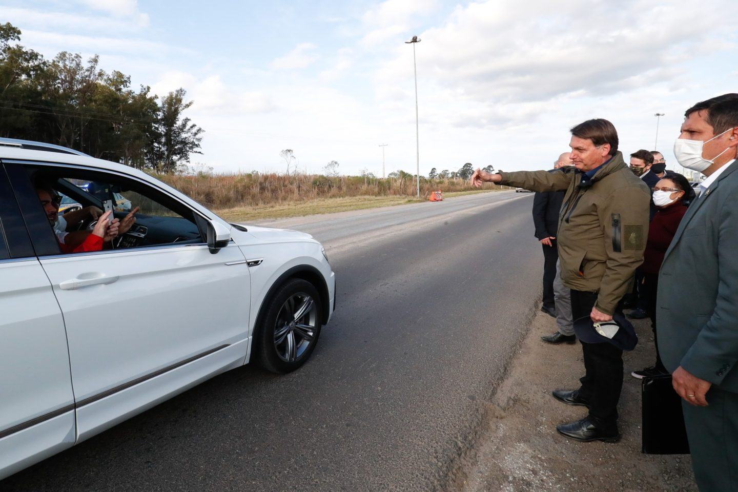 Bolsonaro acena a pessoas dentro de um carro na beira da estrada.