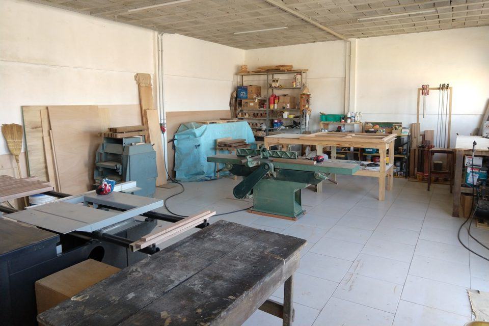 Marcenaria, com duas mesas, uma estante ao fundo e várias máquinas.