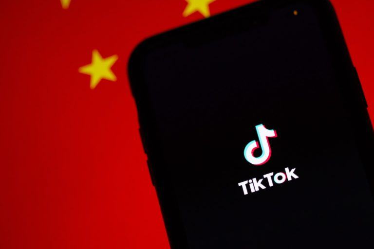 Celular em primeiro plano, com a tela escura e o logo do TikTok, e ao fundo a bandeira da China.