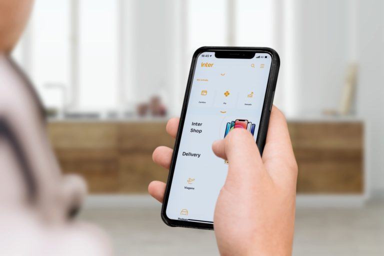 Mão segurando um celular com o aplicativo do Inter aberto.