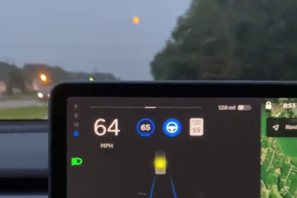 Tela no painel de um Tesla mostrando um semáforo amarelo e, do lado de fora, céu com a Lua ao centro.