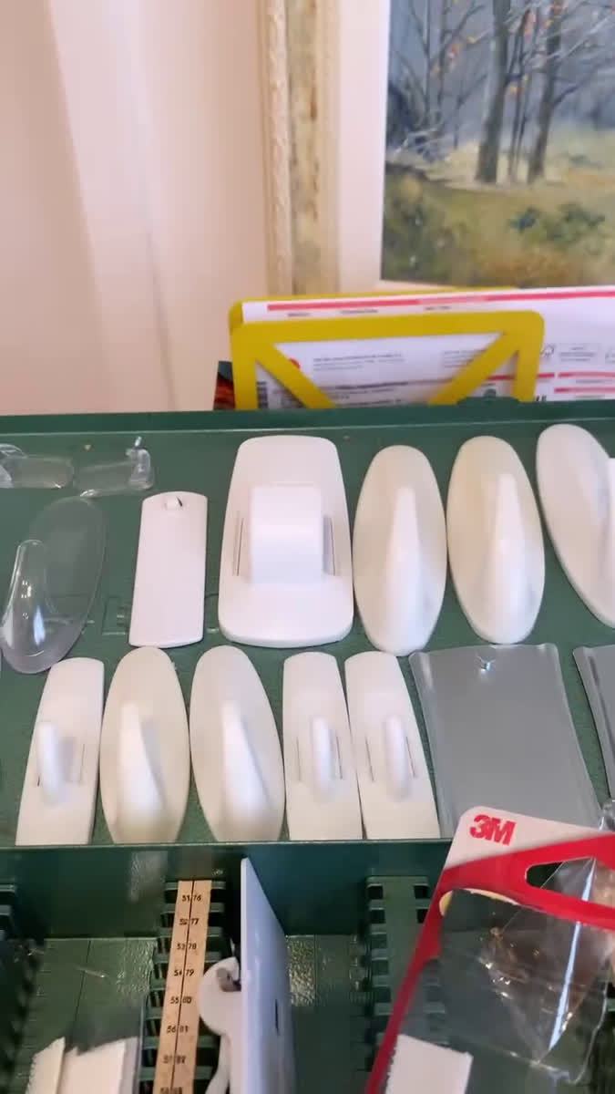 Vários ganchos removíveis, a maioria brancos, sobre uma superfície verde escura.