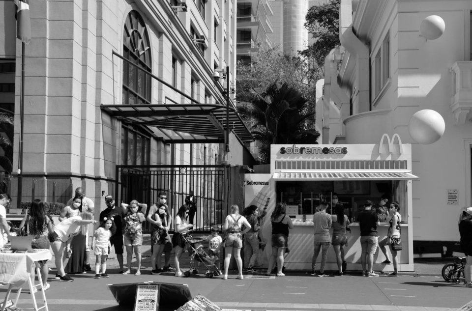 Pessoas em fila, numa calçada, em frente a um quiosque de sorvete do McDonald's.