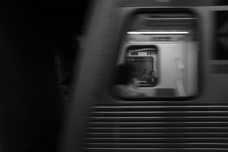 Várias janelas de trens do metrô alinhadas, com algumas pessoas visíveis dentro delas.