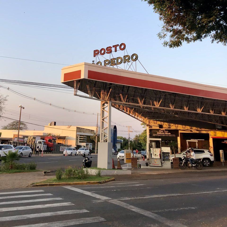 Posto de combustíveis em uma esquina, no fim da tarde, com um letreiro antigo parcialmente coberto pela cobertura escrito “Posto São Pedro”.