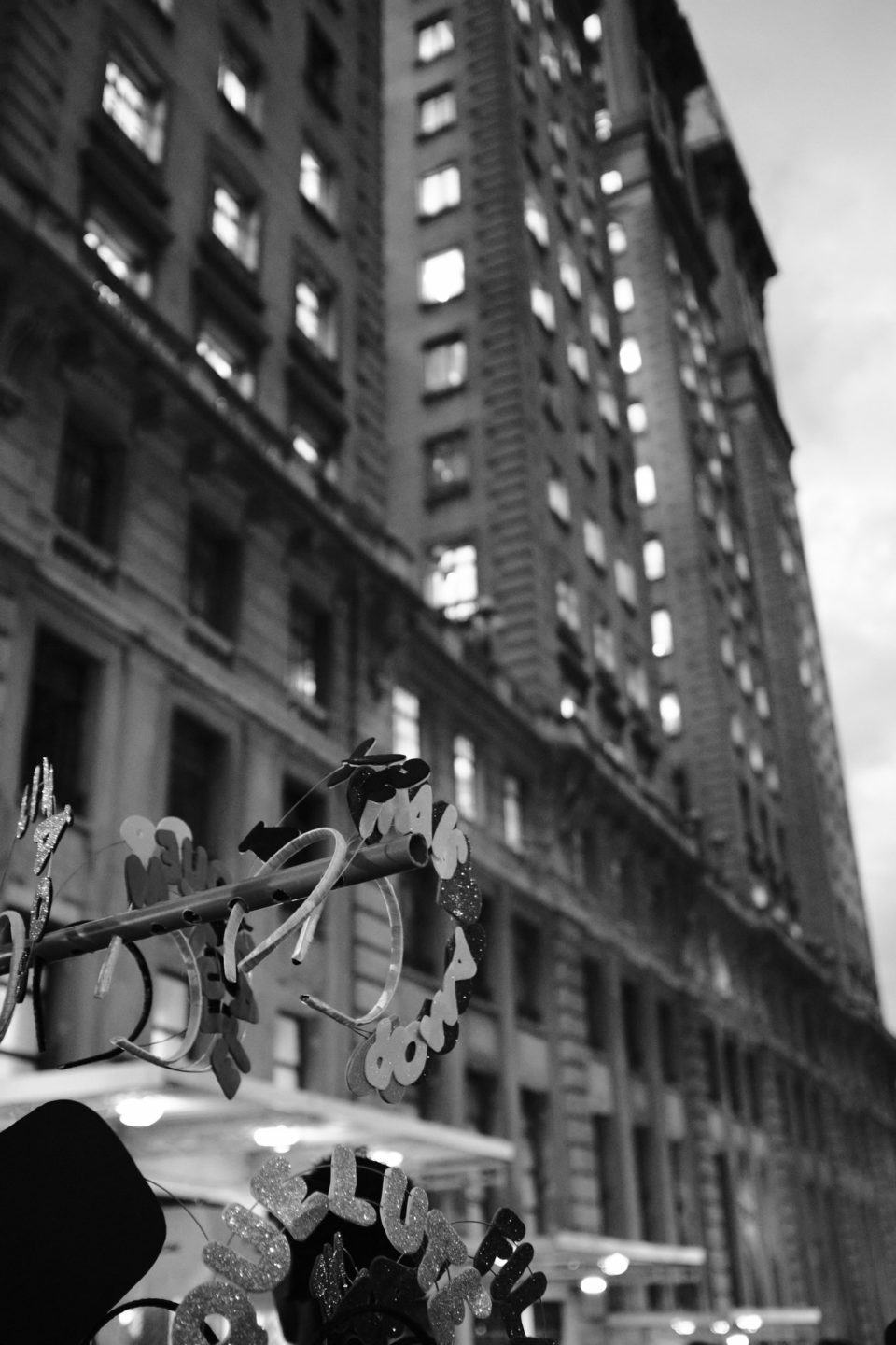 Foto em preto e branco, de alguns arcos de cabelo festivos/carnavalescos em primeiro plano e um grande prédio ao fundo.