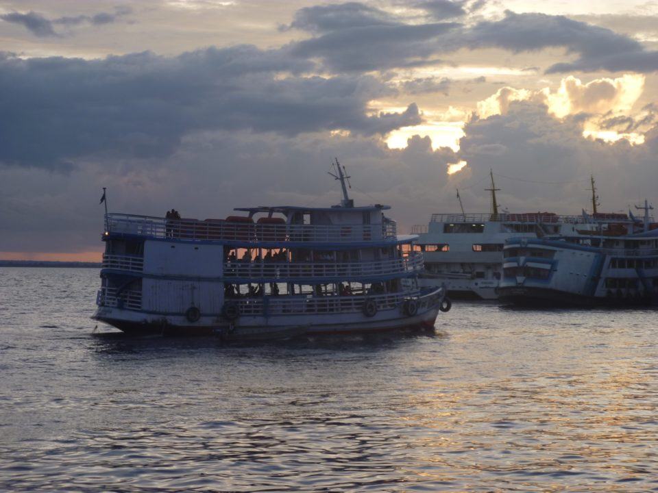 Embarcações em um rio, no entardecer, com céu nublado.