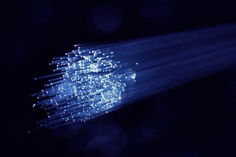 Dezenas de cabos de fibra óptica, com as pontas iluminadas em azul, em um ambiente completamente escuro.