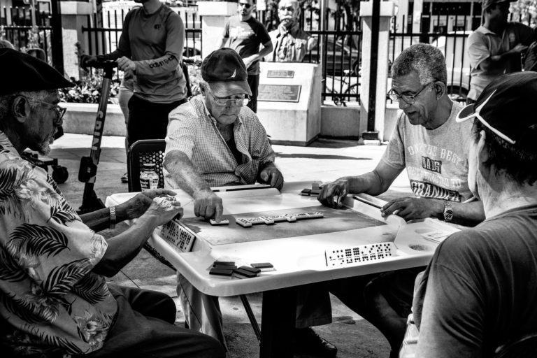Foto em preto e branco de homens idosos jogando dominó ao ar livre.